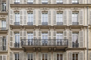 A multi-story building with uniform window shutters and decorative iron railings on balconies. - Joivy Charming 2-bed Flat w/ Shared Spaces (Paris)