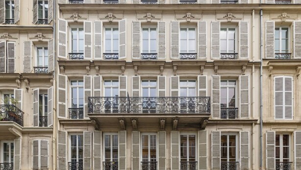 Un edificio a più piani con uno stile architettonico uniforme, caratterizzato da balconi con ringhiere in ferro battuto e persiane.