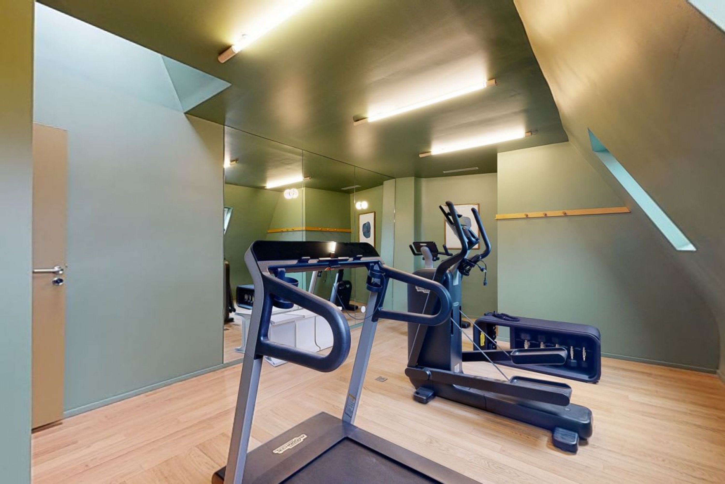 Une salle de sport équipée de tapis de course, de vélos d’exercice et d’un mur recouvert de miroirs.