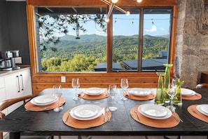 A dining table set for six with a mountain view, wooden walls, and a rustic kitchen area. - Stunning views | Hot tub | Games | 5BR Sleeps 14 (Oakhurst)