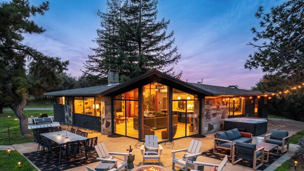 A modern house with a large glass front, outdoor seating, and a fire pit. - Stunning views | Hot tub | Games | 5BR Sleeps 14 (Oakhurst)