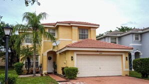 A two-story house with a red-tiled roof, a garage, and a well-maintained lawn. - Home located  10 minute from Hard Rock Stadium Home of the FIFA World Cup 2026  (Miramar)