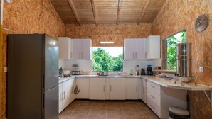 Eine kleine Küche mit Kühlschrank, Schränken, einer Spüle und einem Fenster mit Blick auf Grünflächen.