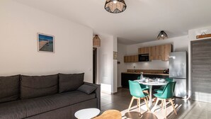 Ein modernes Wohnzimmer mit einem grauen Sofa, einem Holztisch und einem Essbereich mit grünen Stühlen und einem weißen Tisch.