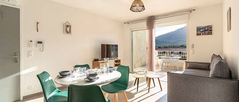 A modern living room with a dining area, a sofa, and a balcony with a mountain view.