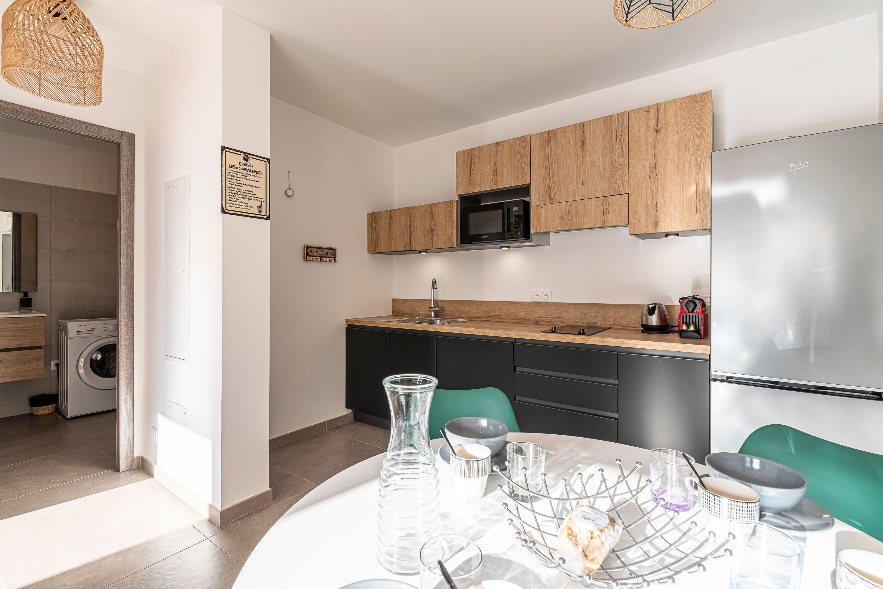 Une cuisine moderne avec des meubles en bois, un réfrigérateur en acier inoxydable et un coin repas avec une table dressée pour deux personnes.