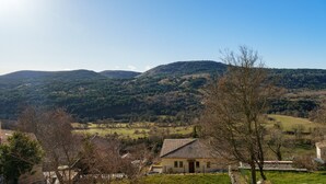 A rural house with a tiled roof, surrounded by trees and a hilly landscape.