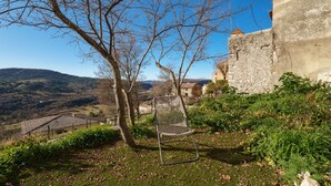 A clear view of a stone building with a sloped roof, surrounded by a grassy area with a metal chair and a tree.