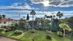 A lush garden with palm trees and various shrubs, a white building with a red roof, and a clear blue sky with clouds. - La Rose des Vents - Cannes (Cannes)