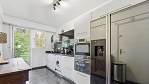 A modern kitchen with a marble floor, built-in appliances, and a large window overlooking greenery. - La Rose des Vents - Cannes (Cannes)