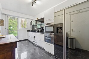 Een moderne keuken met een marmeren vloer, inbouwapparatuur en een groot raam met uitzicht op groen.