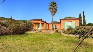 Una casa de dos pisos con techo de tejas, contraventanas verdes y un césped bien cuidado.