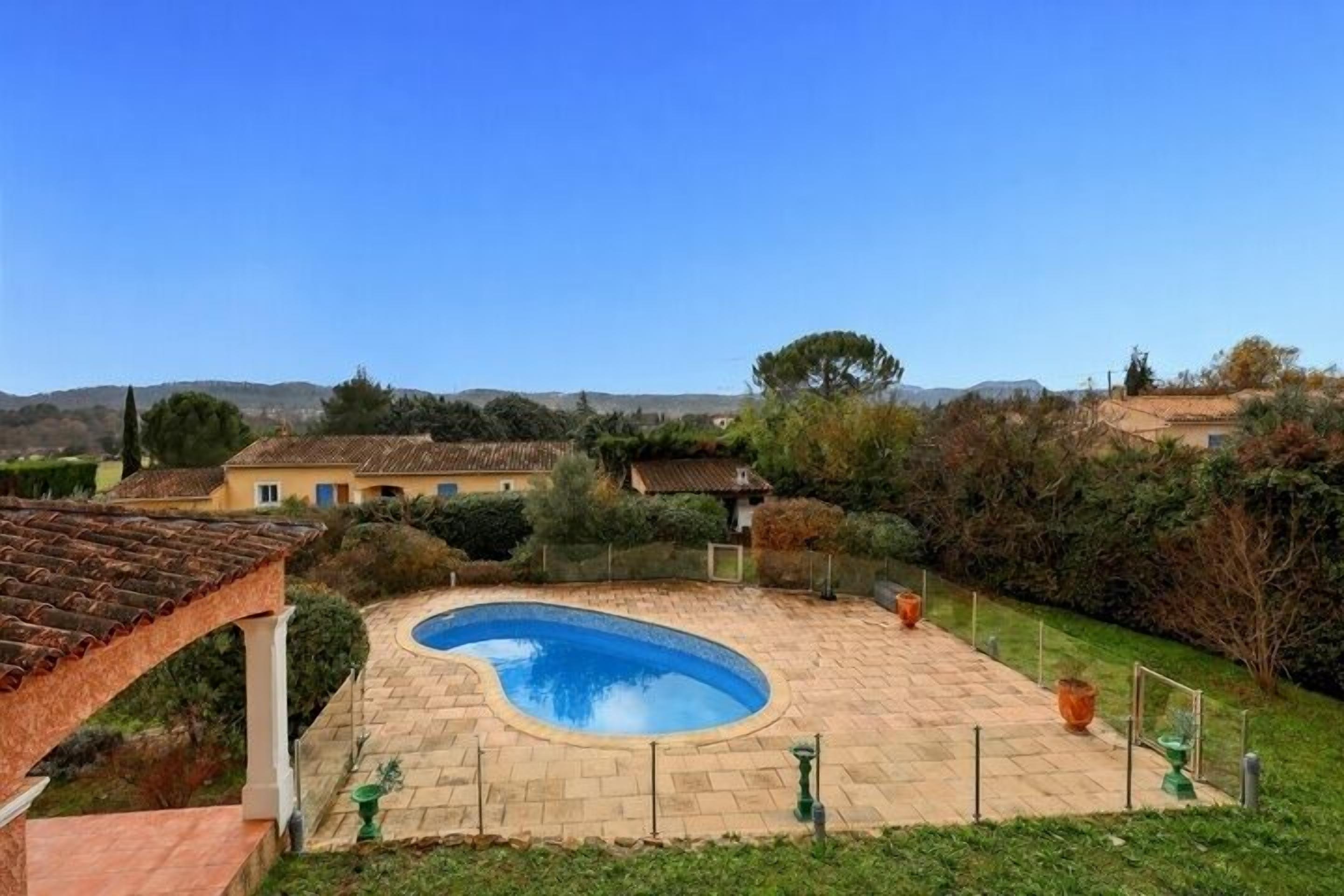 A swimming pool with a curved edge, surrounded by a paved patio and a pergola.