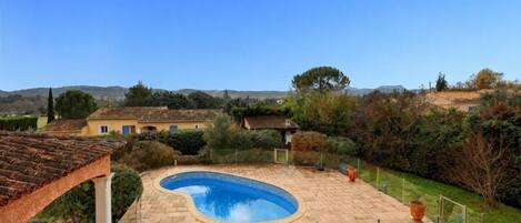 A swimming pool with a curved edge, surrounded by a paved patio and a pergola.