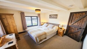 A bedroom with a bed, bedside lamps, a window with curtains, a wooden door, and a painting on the wall. - Honeycott | Sleeps 4 | Croyde Beach (Croyde)