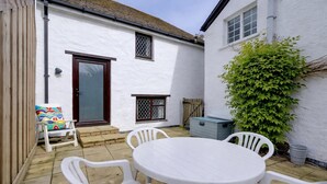 A white building with a tiled patio, a round table, and white plastic chairs. - Honeycott | Sleeps 4 | Croyde Beach (Croyde)