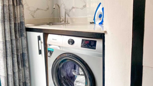 A compact washing machine with a digital display, a sink, and a marble backsplash. - Pazoori Stays at SmartHomes Yaya Centre (Nairobi)