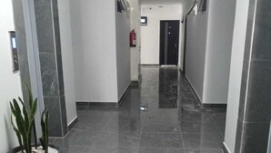 A clean, modern hallway with a marble floor, a potted plant, and a fire extinguisher on the wall. - Pazoori Stays at SmartHomes Yaya Centre (Nairobi)
