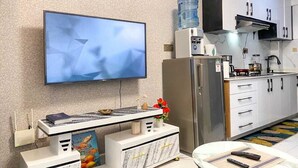 A modern kitchen with a flat-screen TV, a water dispenser, and a refrigerator. - Pazoori Stays at SmartHomes Yaya Centre (Nairobi)