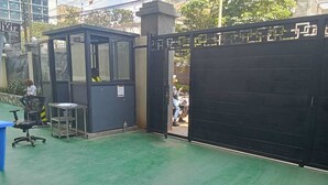 A gated entrance with a security booth, a blue table, and a chair. - Pazoori Stays at SmartHomes Yaya Centre (Nairobi)