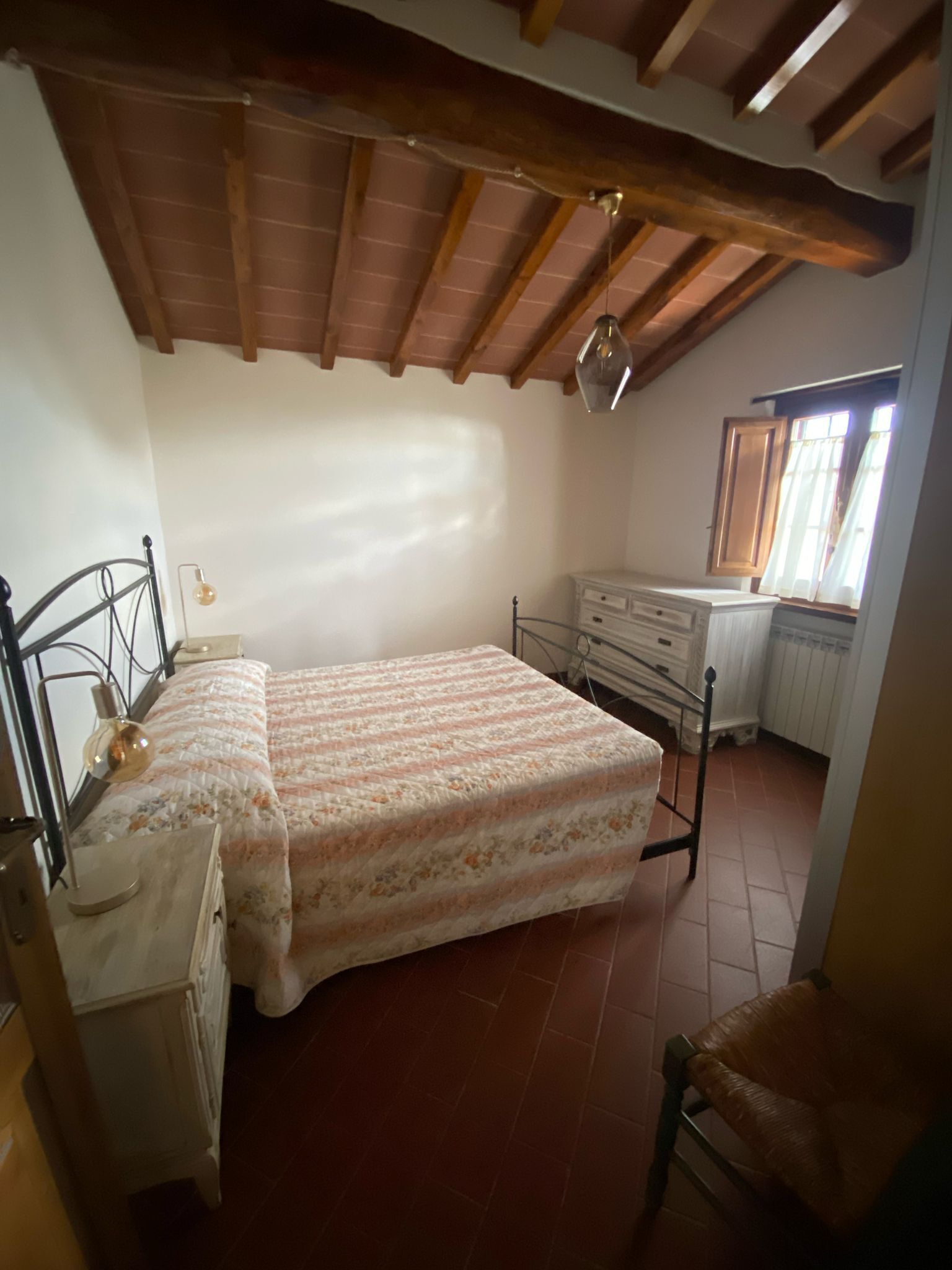 Un dormitorio con cama, cómoda, silla y ventana con cortinas.
