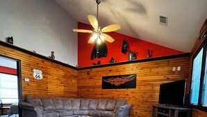 Ein modernes Wohnzimmer mit Ledersofa, Couchtisch, Deckenventilator und einem an der Wand befestigten Fernseher.