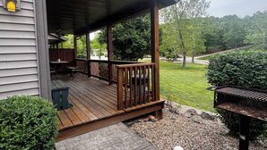 Eine Holzterrasse mit überdachter Veranda, einem Grill und einem kleinen Tisch mit Stühlen.