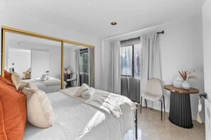 Una camera d'albergo moderna con un letto grande, un tavolino rotondo, una sedia, uno specchio e una finestra con tende.