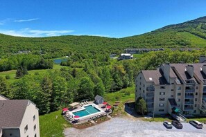 A residential area with a swimming pool, multiple buildings, and a hilly landscape in the background. - BreezelyBruin- Shuttle on shuttle off pool Hot tub (Killington)
