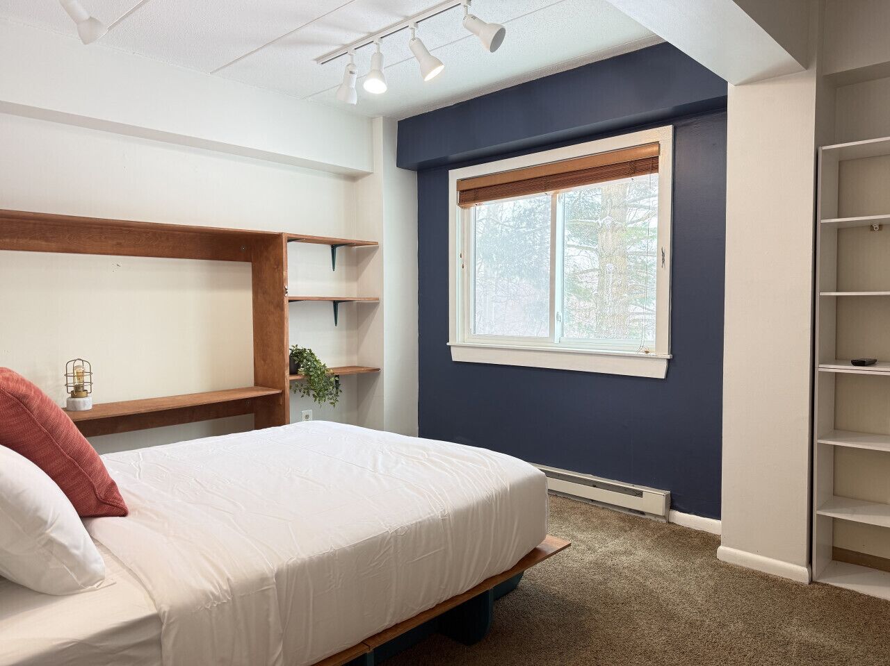 Une chambre à coucher comprenant un lit, une fenêtre, une étagère et un radiateur.