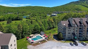 Et boligområde med swimmingpool, flere bygninger og et bakket landskab i baggrunden.