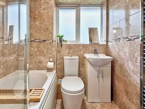 A bathroom with a bathtub, toilet, and sink, featuring marble tiles and a window. - Charming 3 bedroom house in Chelmsford (Essex)
