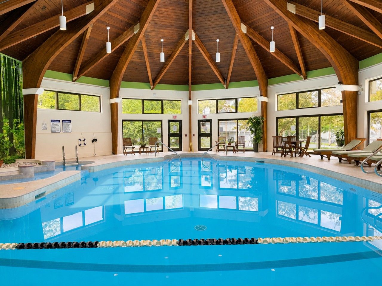 Une piscine intérieure avec des poutres en bois, de grandes fenêtres et des chaises longues.