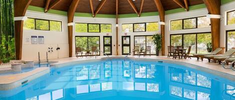 An indoor swimming pool with wooden beams, clear windows, and lounge chairs.