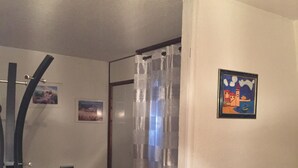 Un dormitorio con una cama, un televisor, un escritorio con una impresora y una puerta que da a otra habitación.