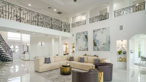 Amplia sala de estar con un sofá seccional beige grande, dos mesas de centro redondas oscuras y una escalera con barandales negros ornamentados.