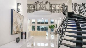 Un vestíbulo amplio con una escalera moderna, un cuadro abstracto de gran tamaño y una zona de estar con vistas al exterior.