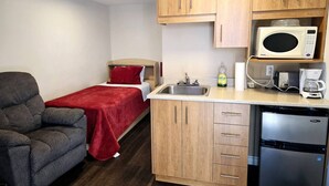 Une chambre compacte comprenant un lit, un canapé, une kitchenette équipée d’un four à micro-ondes, d’une machine à café et d’un lave-vaisselle.