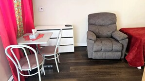 Une petite pièce comprenant une table à manger, deux chaises, un fauteuil gris et un rideau rouge.