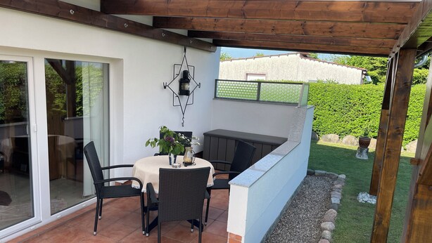 An outdoor patio with a table, chairs, a small grill, and a decorative wall-mounted light fixture.