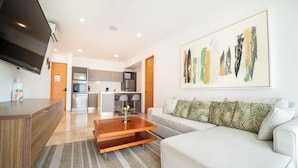 A modern living room with a sofa, a coffee table, and a TV. There is a kitchen in the background with a dining area. - 2 BR Condo Rooftop Ocean View - Sasha I (Playa del Carmen)
