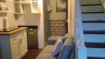 A compact living space with a kitchenette, a sofa, and a staircase.