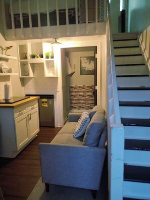 A compact living space with a kitchenette, a sofa, and a staircase. - The Tiny Nook in Downtown + Free Parking (Raleigh)