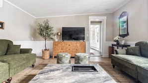 A living room with a large marble coffee table, two green sofas, a wooden cabinet, and a flat-screen TV. - Designer Cottage • Game Room w/PacMan • Mins to Beach (Kennebunk)