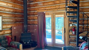 L’intérieur d’une cabane en rondins, avec un escalier en bois, une cheminée, un canapé et un coin repas.