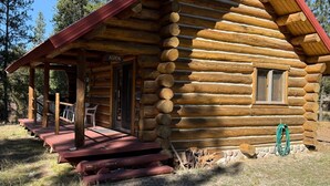 Une cabane en rondins avec un toit rouge, une cheminée et une véranda dotée de sièges pour l’extérieur.
