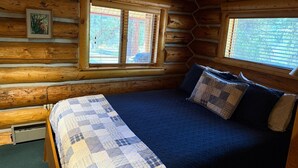 Une chambre am énagée dans un chalet en rondins, avec un lit, deux fenêtres et un tableau au mur.