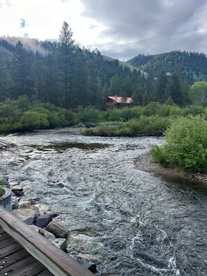 Une rivière avec un pont en bois au premier plan, entourée d’une forêt dense et, au loin, une montagne.
