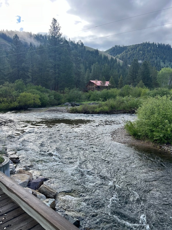 A river with a wooden bridge in the foreground, surrounded by dense forest and a mountain in the background. - Riverside Romance & Adventure at the Aspen Cabin on the Alta Ranch (Darby)
