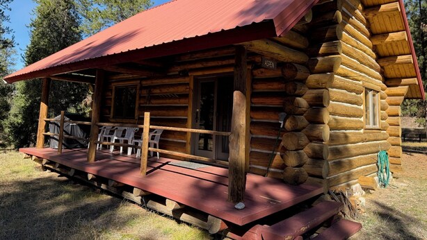 Une cabane en rondins avec un toit rouge, une terrasse en bois et une cheminée.